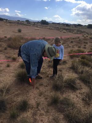 11-LOA-2018 MIAC Research Associate Leon Natker assists a young visitor is finding artifacts on the survey course designed to teach visitors the importance of recording artifact locations and the difficulty of recording surface collections. Photographer: 